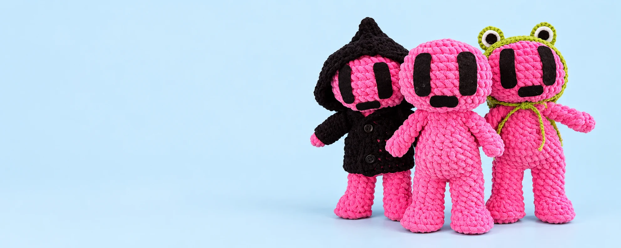 Três amigurumis rosa: um com roupa de bruxinha, um sem fantasia e outro com capuz de sapinho