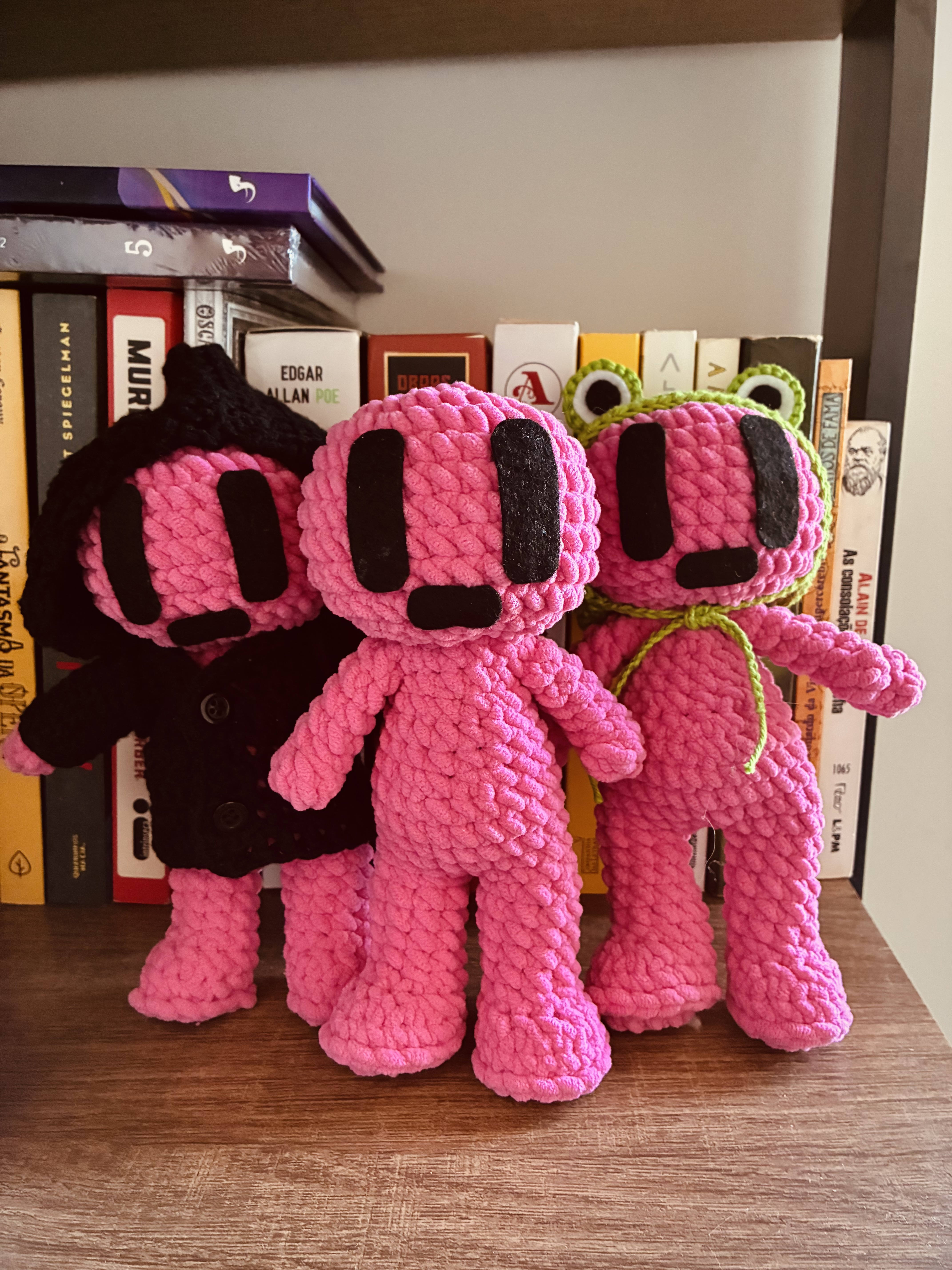 Três amigurumis rosa Bapo diante de uma estante de livros